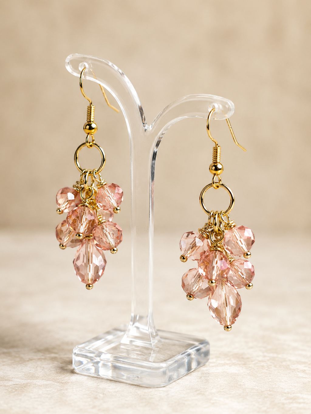 Pink crystal earrings on a clear stand with a beige background