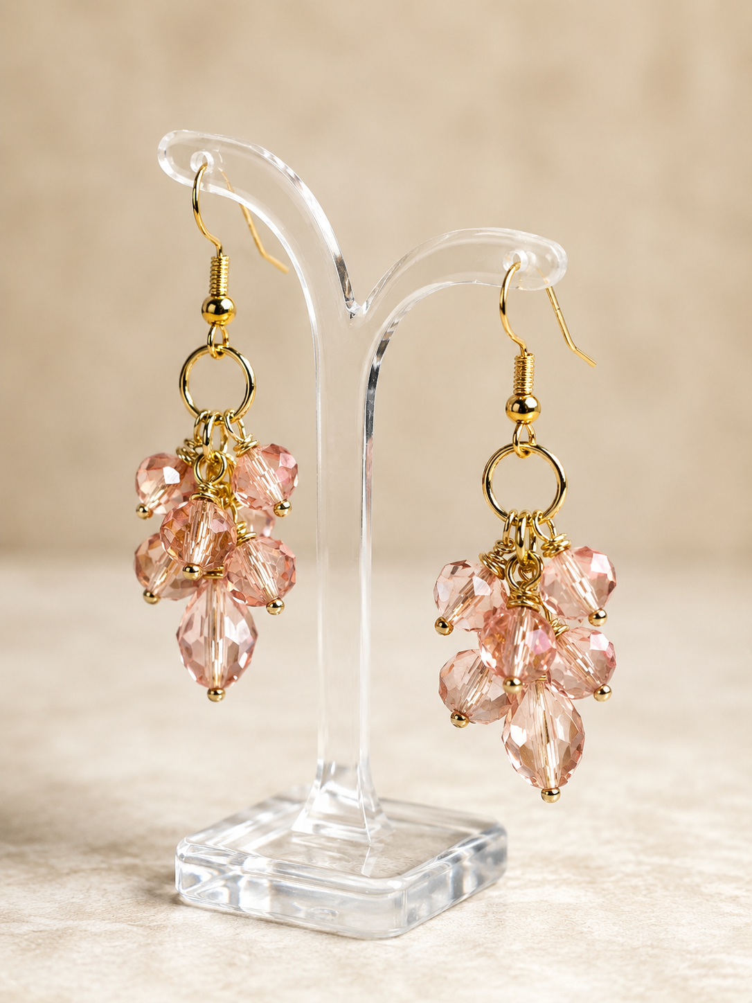 Pink crystal earrings on a clear stand with a beige background